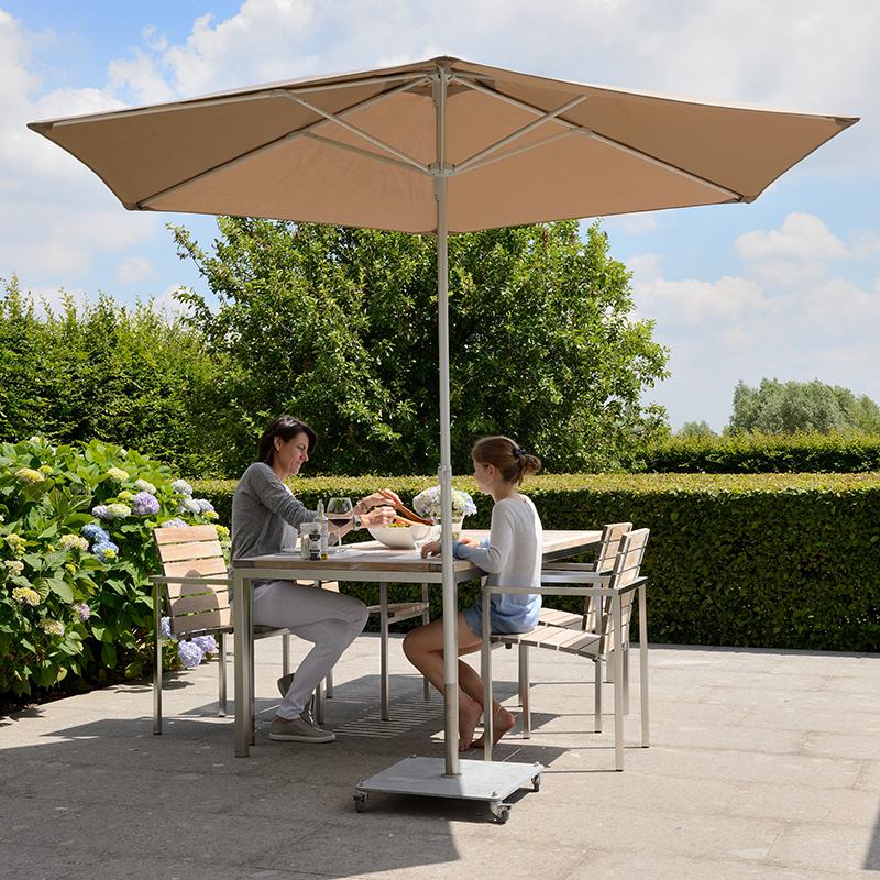 Orange parasol henover et sæt havemøbler, hvor en kvinder og en pige sidder og spiser.