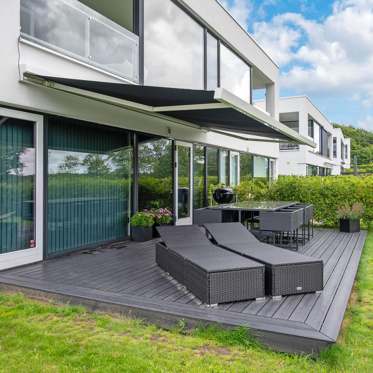 Markise på et hvidt hus ved en terrasse, hvor der står to solsenge.