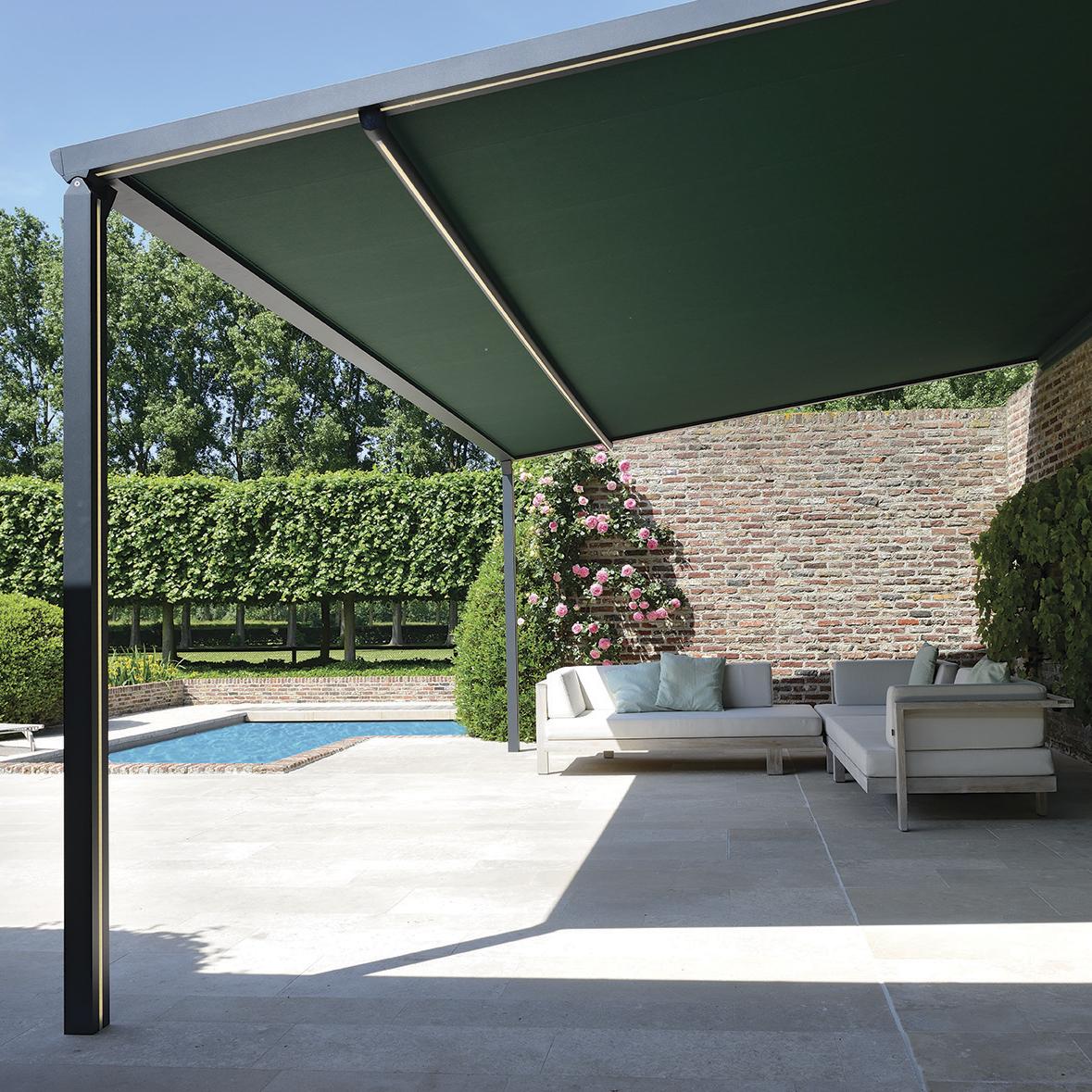 Pergola B-128 der står ud fra huset og overdækker terrassen, hvor der står havemøbler.