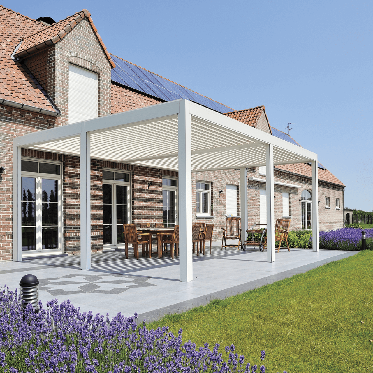 Pergola med hvide lameller der står ud fra huset og overdækker en stor terrasse.