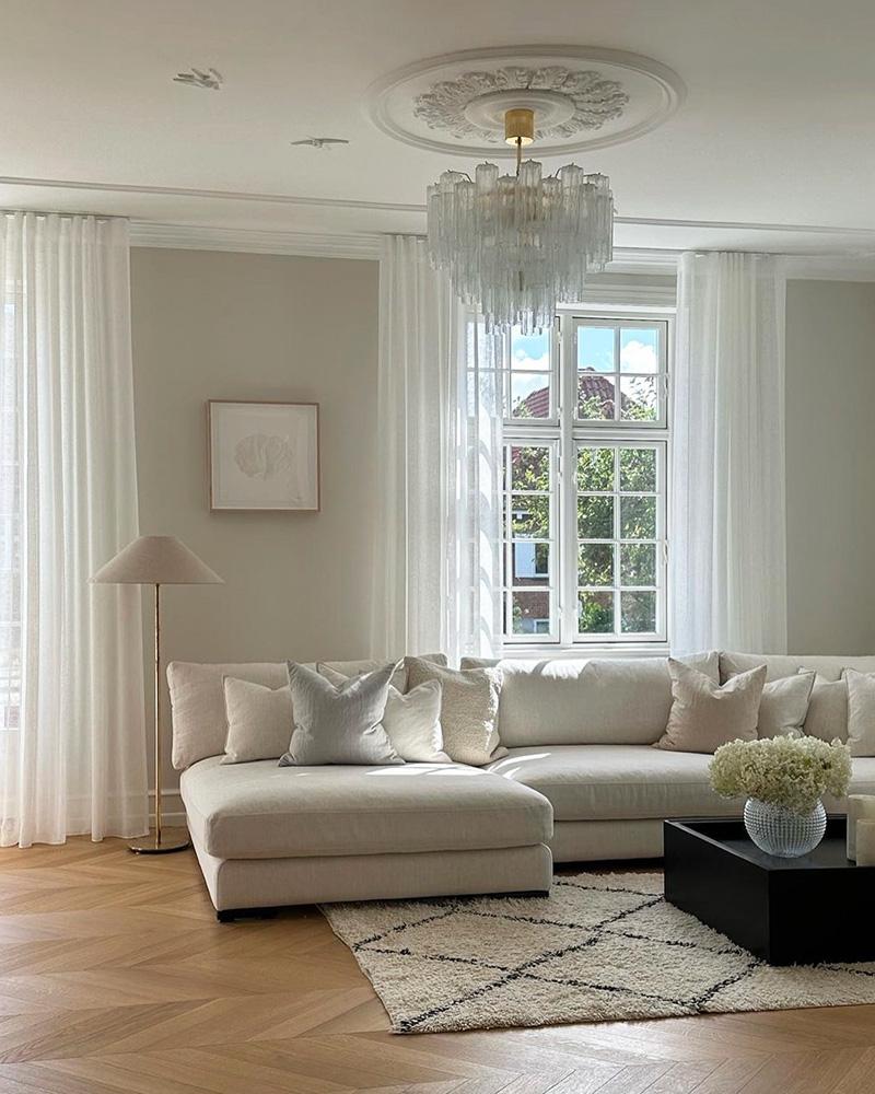 Lys stue med lys beige sofa og lette hvide stofgardiner bagved